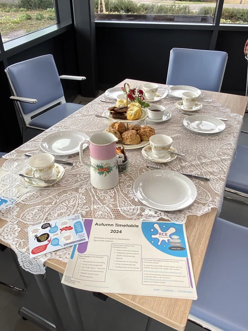 A beautifully presented table with fine china, scones, tea, and some RCE Wellbeing Hub promotional material