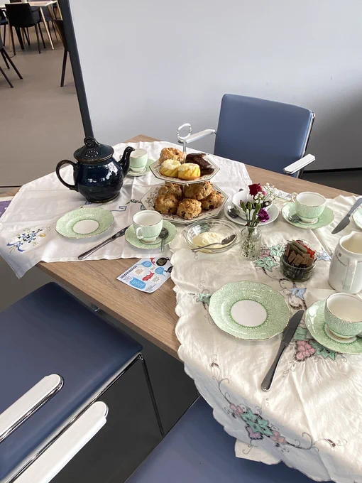 A beautifully presented table with fine china, scones, tea, and some RCE Wellbeing Hub promotional material