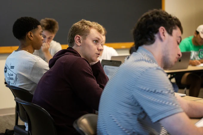 Three students in foreground listen to the lecture.