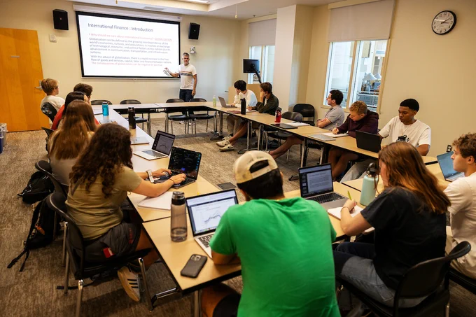 Students in small seminar room listen to Professor Riera-Crichton present on the first day of class for International Finance.