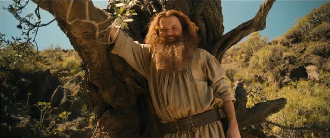 Picture of  a smiling Tom Bombadil leaning against an olive tree