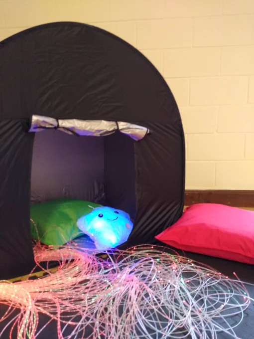 A photo of a dark tent with cushions, light strings and a fluffy light up star cushion inside.