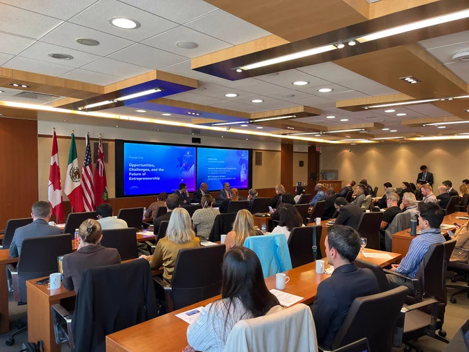 Large view photo of a conference room with participants listening to panelists at the front of the room. 