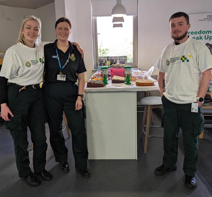 Three NHS staff members standing behind a table with baked goods.