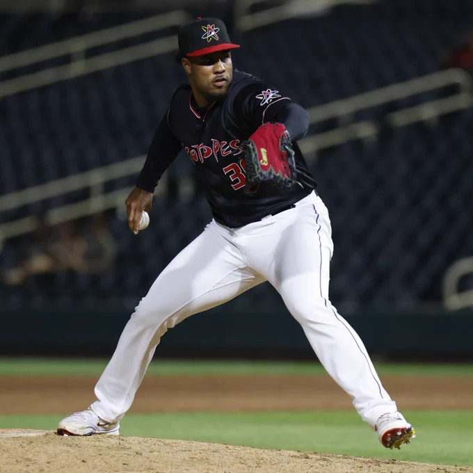 Jaden Hill winds up to throw a pitch in a black Isotopes uniform