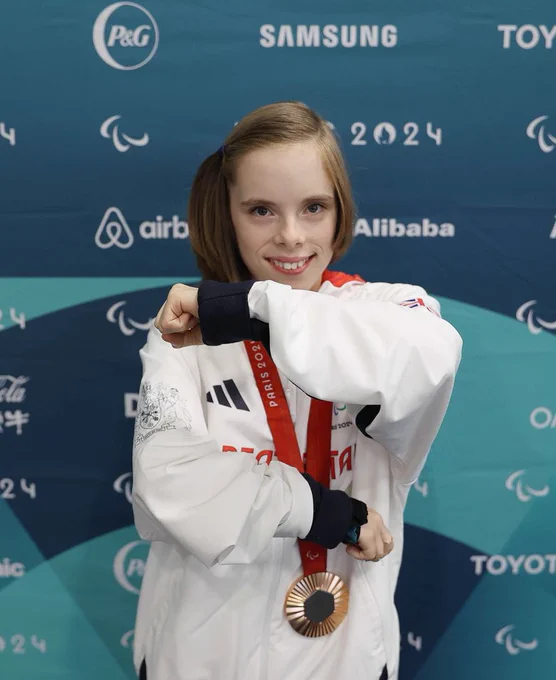 Bly doing the equals sign with her arms with her medal