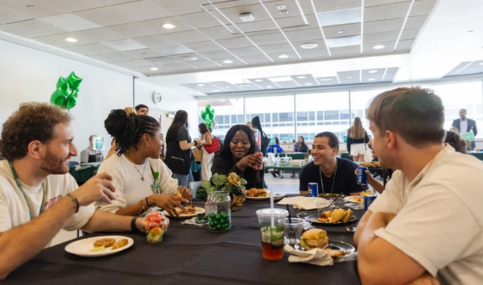 A group of Rush University students People enjoying food and conversations at a cafeteria-style table.