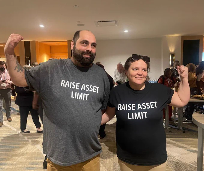 A man and woman wear matching t-shirts that say "RAISE ASSET LIMIT." They are standing side-by-side with their arm around each other and flexing their other arm to indicate strength.