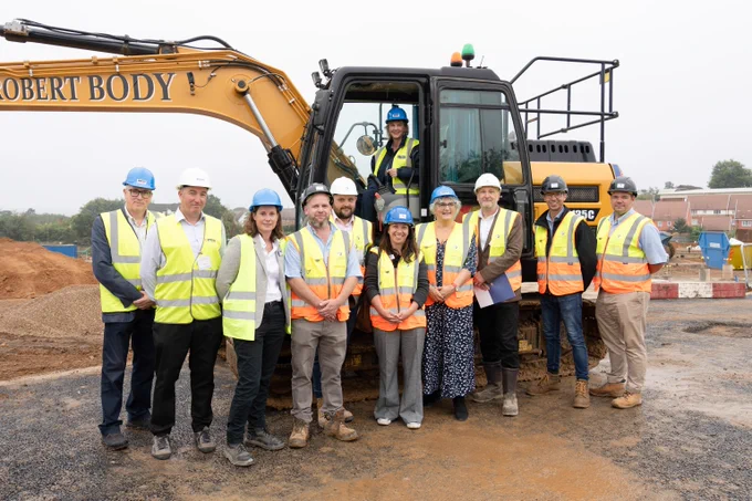 A picture of West Kent and Penenden Heath Development colleagues outside of a yellow digger on a building site in Allington.