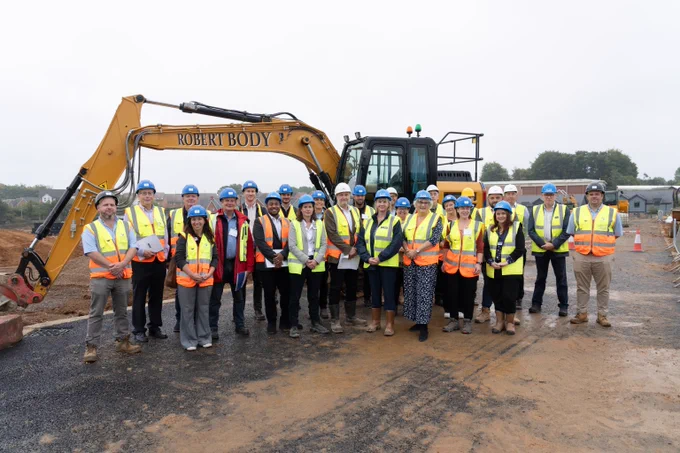 A picture of West Kent and Penenden Heath Development colleagues and partners outside of a yellow digger on a building site in Allington.