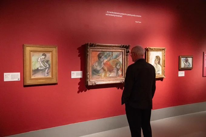 Photography by Paul Watt Photography. Man in black suit stands against red exhibition wall