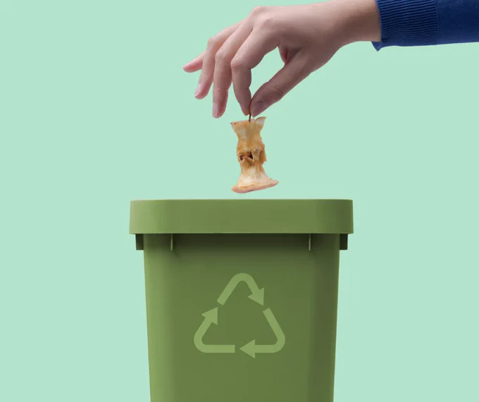 A person throwing an apple core into an organics recycling cart