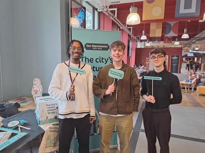 An image of three young men at an Our Manchester engagement event holding up post it notes which say #ShapeOurManchester, The city's future - shaped by me! and Our Manchester. 