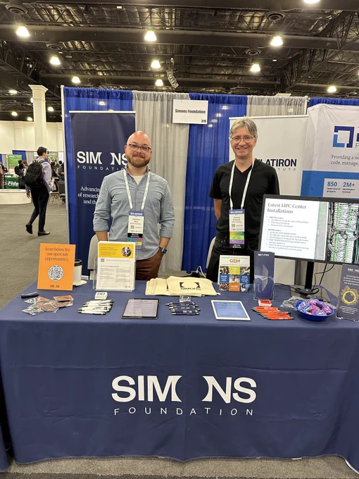 Two Simons Foundation employees stand behind a blue tablecloth at a recruitment booth