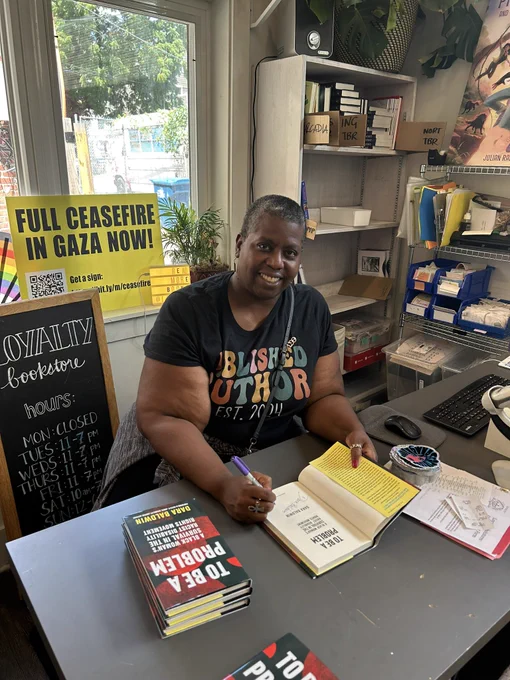 Woman in book store sits at table signing books.