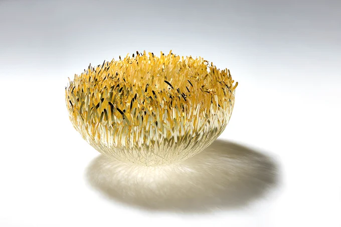 A brooch made of small thin metal gold leaves clustered together in a rounded gathering.