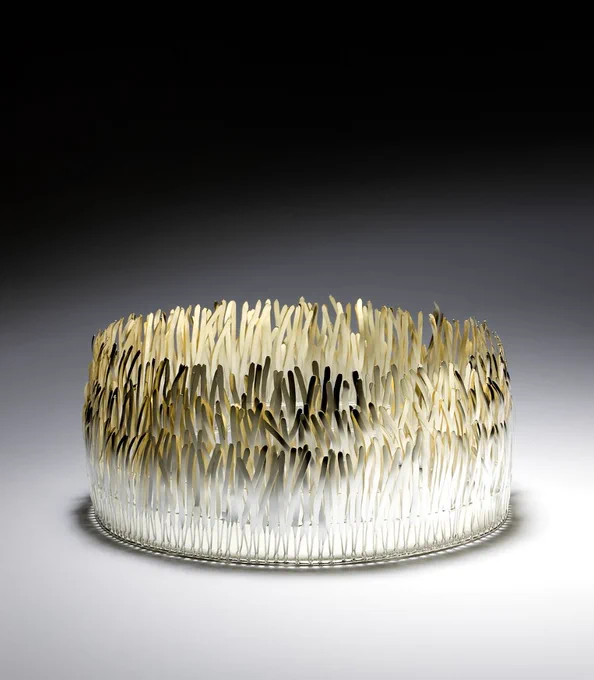 Thin metal wires are clustered together, shaped like feathers or leaves, arranges in a circle to resemble a ringed or crown of a forest.