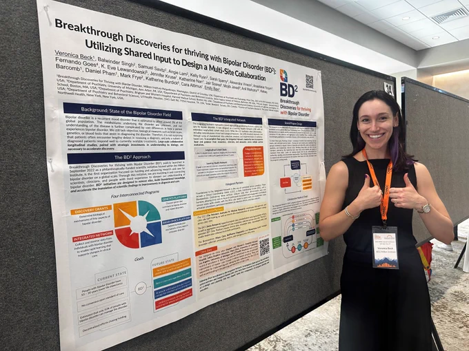 Veronica Beck standing in front of BD²'s poster at the 2024 NNDC Annual Conference, smiling and giving two thumbs up.