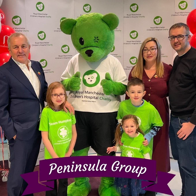 Peninsula Group image. A green teddy bear in the middle wearing Manchester Children's Hospital clothes, with a family stood around it.