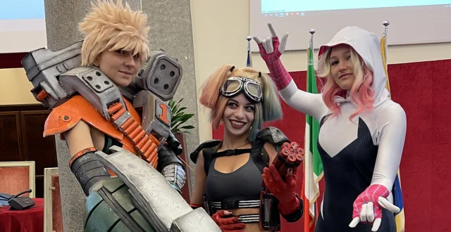 Tre cosplayer, due ragazze e un ragazzo: lui ha capelli biondi corti e un braccio meccanico, una ragazza ha della dinamite in mano e l'altra ha capelli biondi e rosa e una tuta bianca e nera con cappuccio