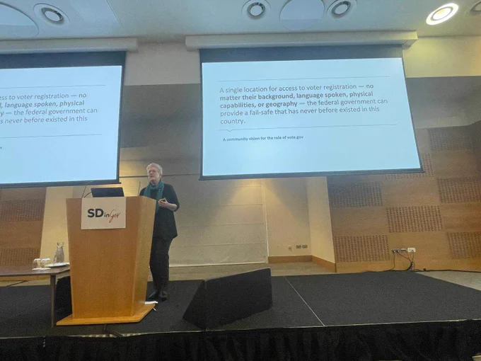 A person in front of an audience conference room presenting. 