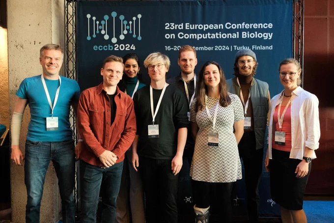 Group photo in front of the ECCB banner. Smiling faces from left: Bernhard Renard, Julian Zabbarov, Ferdous Nasri, Yannick Hartmaring, Tobias Pietz, Marta Lemanczyk, Simon Witzke, and Katharina Baum.