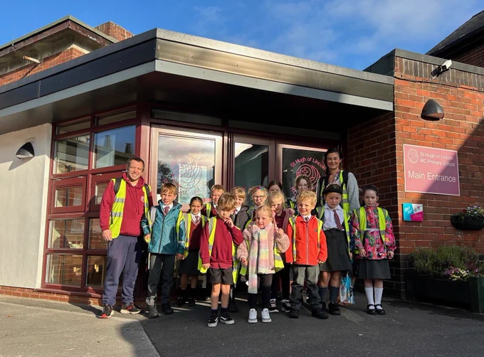 A group of children and two teachers pose in front of a primary school