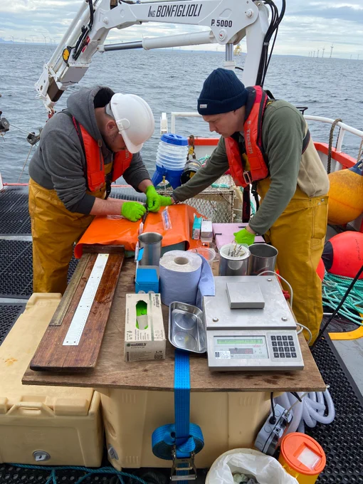 Two scientists working over a table with equipment on it on a boat. 