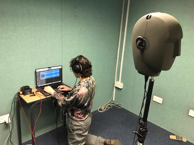 A person working on a laptop near a grey sponge microphone head
