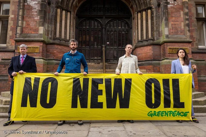 Four activists stand in front of the courthouse holding a big yellow banner that says: NO NEW OIL