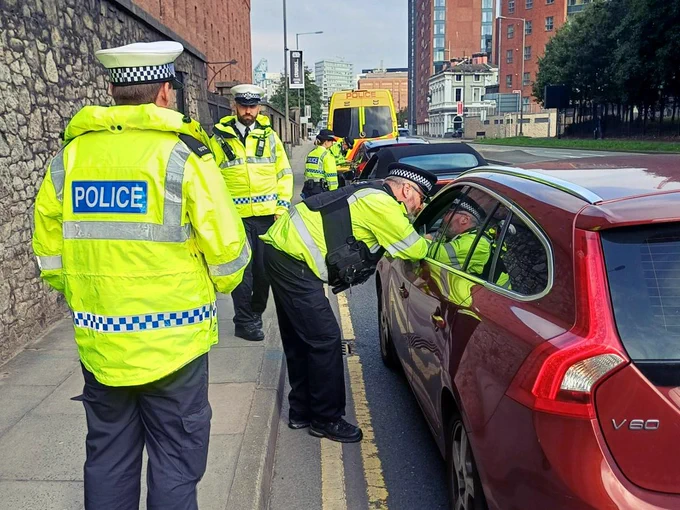 Project Servator officers at a vehicle checkpoint, supported by colleagues from the Roads Policing Unit. Officers are engaging with the occupants of vehicles that have been stopped at the checkpoint.