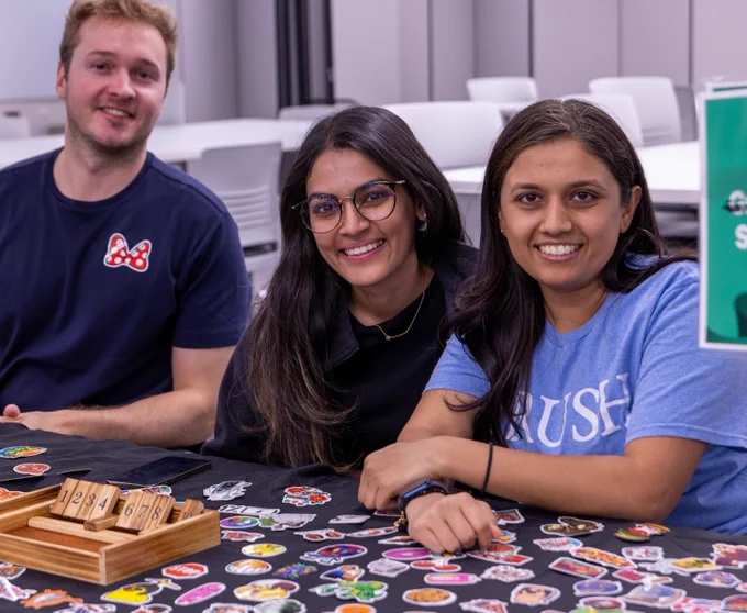 Three smiling Rush students sitting around a table adorned with stickers.