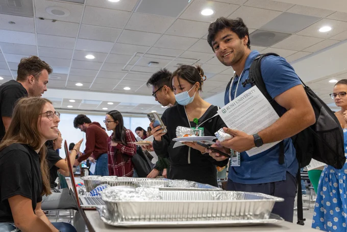 Rush University students interacting and selecting food from buffet trays.