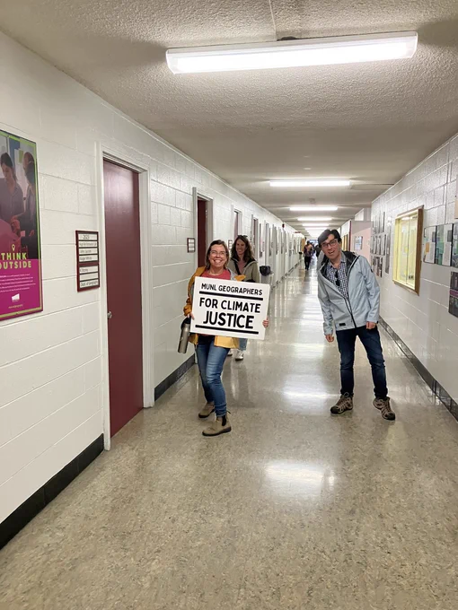 Geography faculty walk down the hall to the climate strike holding a sign that says “MUN Geographers for climate justice”