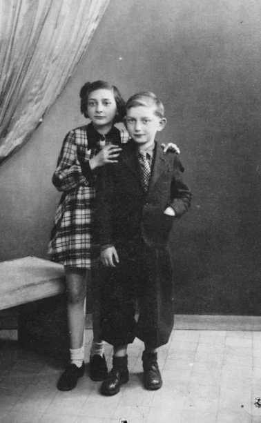 Vintage black and white photo showing two young individuals in formal attire, standing close together in a studio setting. 