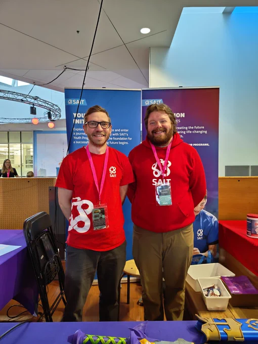 Two individuals in branded T-shirts standing at a SAIT booth in front of a blue backdrop.