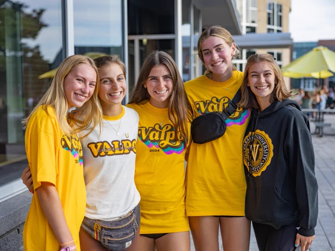 Five students wearing Valpo gear smile as they pose for a photo together in front of the Harre Union.