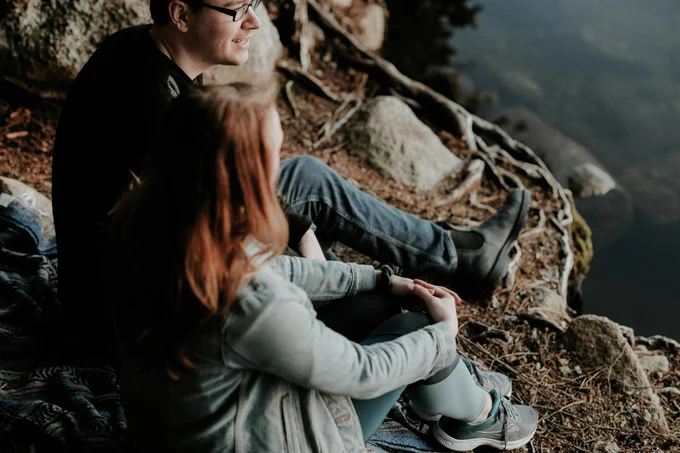 Two people sitting chatting in the banks of a river.