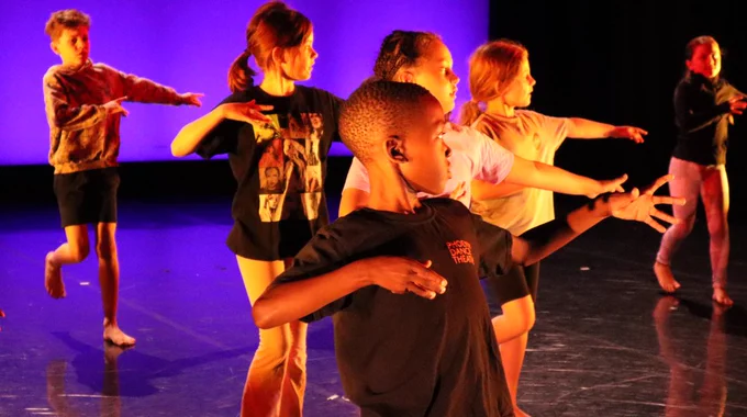 Young dancers performing on purple lit stage. Each dancer shares the same dance pose as left arm is central and right arm is out.