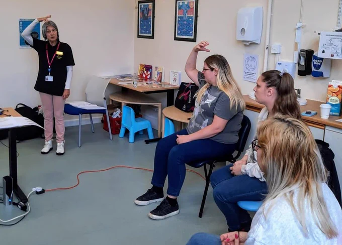 Helene stands in front of a group of parents, teaching Makaton to aid in family communication