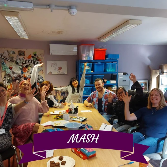 Image of MASH volunteers around a table raising their arms and smiling at the camera.