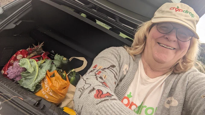 A selfie of the driving volunteer with the donated vegetables in the boot of her car. She is smiling whilst wearing a CropDrop branded hat and t-shirt.