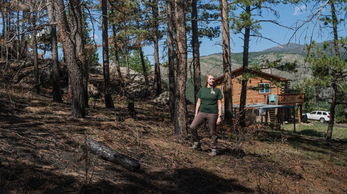 Woman standing on the edge of burned forest near log home