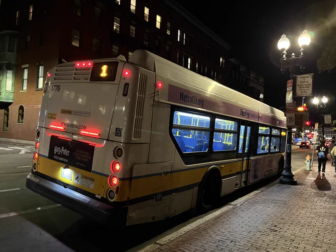 An MBTA bus is seen pulled over on the side of the street in Harvard Square, Cambridge. The rear digital route sign reads "1".