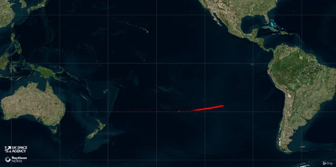 Satellite image displaying a map of the Earth with a focus on the Pacific Ocean. A red arrow stretches across the ocean, indicating re-entry path. Notable continents visible include parts of South America, North America, and Australia. 