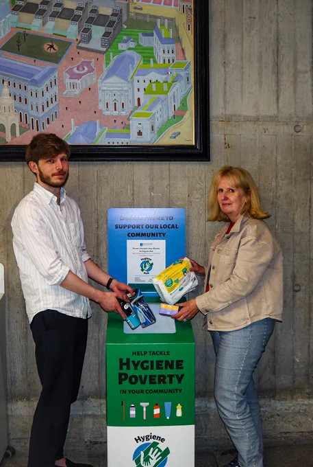 Library staff Joe Yeates and Iris Bedford Library colleague holding hygiene products in front of the drop off box in the Library foyer (former Berkeley Library)