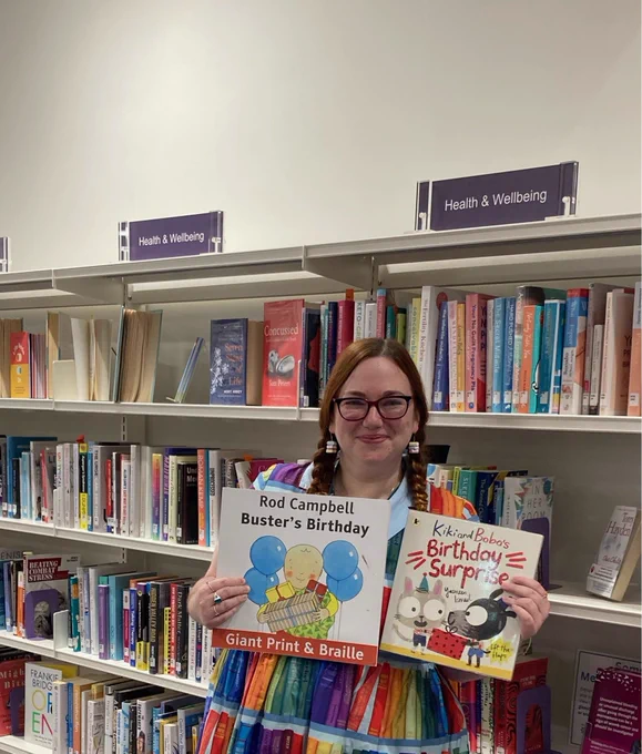 Girl in rainbow book shelf dress holding two children's books against a backdrop of books.