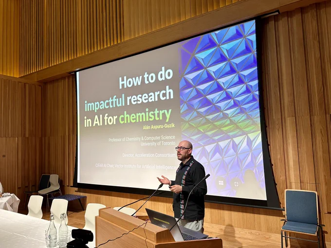 A photo of Alán Aspuru-Guzik in front of his title slide