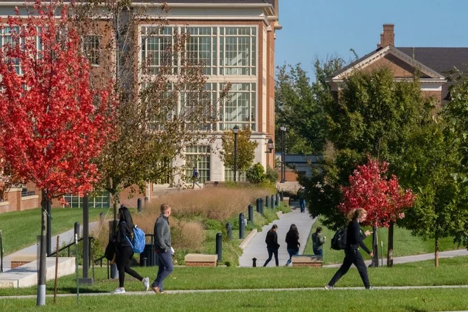 The psychology building on an idyllic campus with maple trees turning read and students walking around