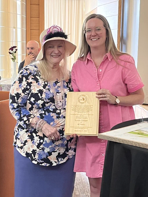 Two women standing together, holding a wooden plaque.